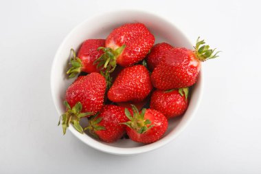 Bir grup canlı kırmızı çileğin beyaz arkaplandaki bir kasede çekilmiş yakın çekim görüntüsü.