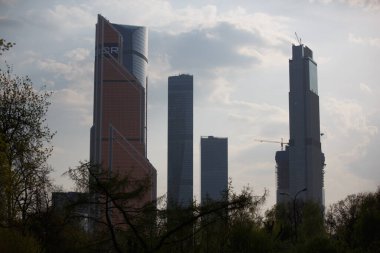 MOSCOW / RUSSIA - 20 / 04 / 2019 dikey uzak şehir manzarası Moskova gökdelenlerinin tepeleri uzun ağaçların, dalların, yeşil yaprakların arkasına gizlenmiş. Fotoğraf: Krasnaya Presnya Şehir Parkı