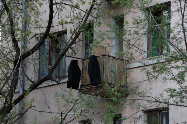 在一座古老的苏联式住宅的阳台上 两个黑色外套和夹克在阳光下挂着晒干 窗户被树枝上的绿叶遮掩着 — 图库照片