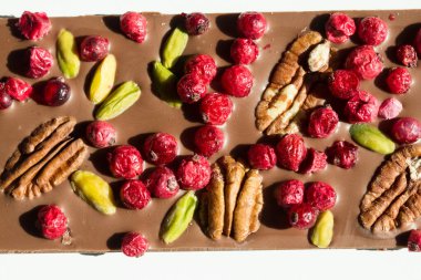 Beyaz arka planda kızılcık, fındık ve şam fıstıklı çikolata.