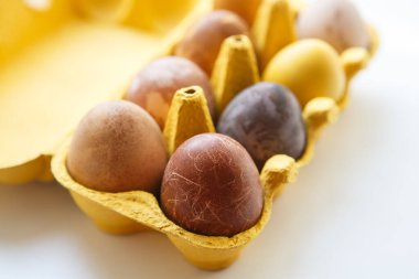 Sarı bir kutunun üst görüntüsünde sekiz farklı renkte ejderha ya da dinozor tavuk gibi görünüyor doğal ürünlerle boyanmış Paskalya yumurtaları (kırmızı şarap, çay, kahve, havuç, zerdeçal, soya sosu)