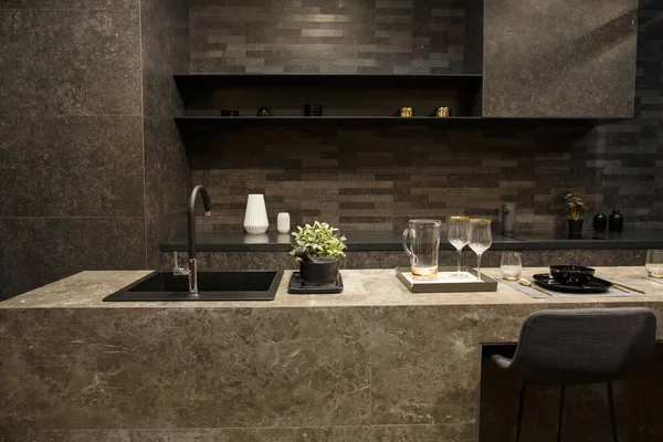 MOSCOW / RUSSIA - 04/03/2019 luxurious spacious modern kitchen island in black grey brown stone marble tones, a sink, a comfortable dining area. a table, wine glasses, plates on the counter top