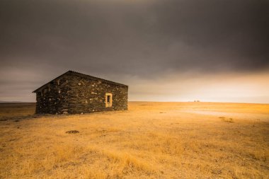 Güneşin doğuşunda bulutlu bir gökyüzü olan bir çiftlikte terk edilmiş eski bir kulübe.