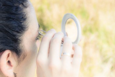 Bir kızın aynanın önünde kaşlarını yolarken yakın plan fotoğrafı.