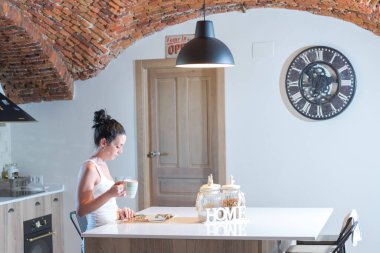 Genç esmer kız mutfakta kahve içerken dergi okuyor.