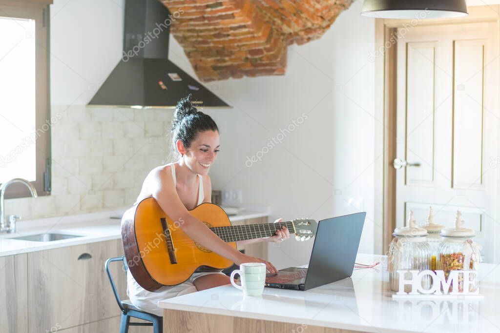 young brunette girl taking online guitar lessons on the couch at home
