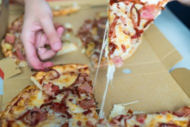 Erimiş peynirli bir dilim pizzayı el topluyor. Yemek siparişi verin..