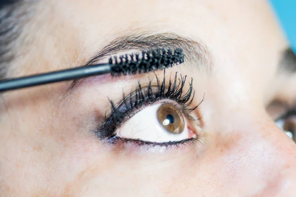 Close-up of the eye of a young woman in profile putting on makeup with mascara for eyelashes