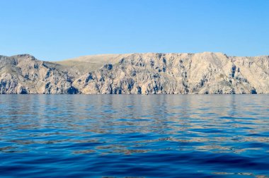 Dalgalanan denizde açık mavi gökyüzü olan çorak kayalar.