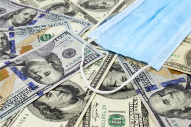 Tıbbi maskeli bir yığın dolar banknot. ABD 'de koronavirüs salgını. COVID-19 'un Amerika Birleşik Devletleri' ndeki mali etkileri.