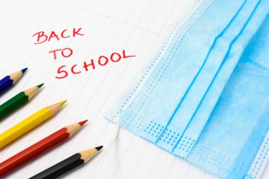 Corona virüsü salgını sırasında okula döndüm. Beyaz arkaplanda izole edilmiş renkli kalemler. Tıbbi yüz maskesi.