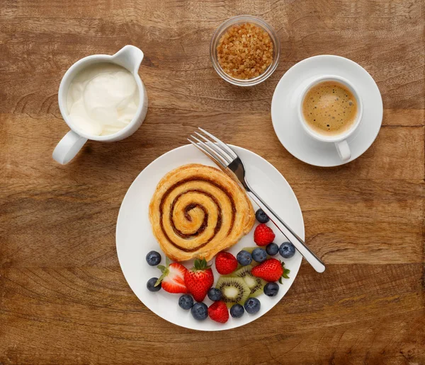 A healthy breakfast of a Cinnamon Swirl, fruit and coffee, shot on a wooden background, from above.
