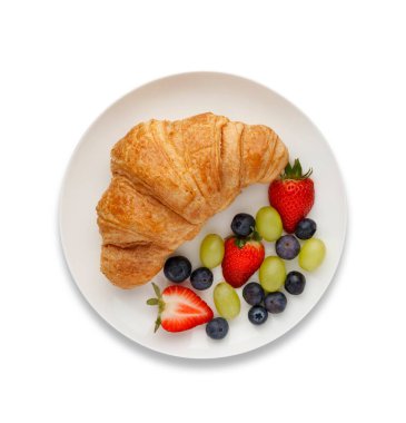 Bir kruvasan ve meyvenin kıtasal kahvaltısı, yukarıdan çekilmiş, beyaz üzerine bir damla gölgesi olan.