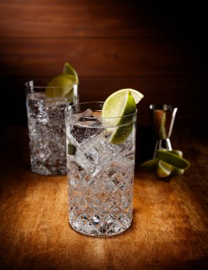 İki kristal bardaktaki spot ışığı Cin ve tonik kokteyli, limon garnitürlü, antika ahşap bir masanın üstünde..