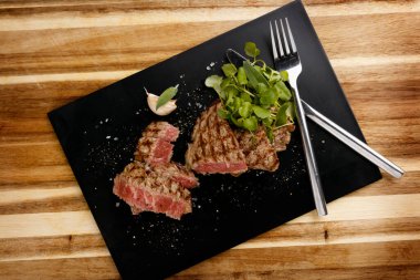 Sulu ve sulu, az pişmiş biftek, su teresi süslemeli, tahta tabakta, bıçak ve çatalla.