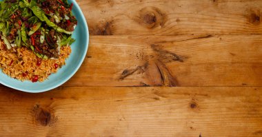 Bir kase leziz Baharatlı Biftek Lettus pirinç yatağına sarılmış ahşap bir zemin ve kopyalanacak yer olan afiş formatında.