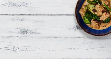 Mavi bir kase sulu Tayland usulü kırmızı tavuk, beyaz ahşap bir zemin ve fotokopi için yeri olan bir pankart vurdu.