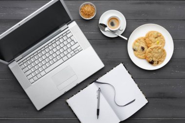 Laptop, kahve, kurabiye ve siyah ahşap arka planda not defteriyle kahve molası veriyorum.