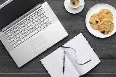 Laptop, kahve, kurabiye ve siyah ahşap arka planda not defteriyle kahve molası veriyorum.