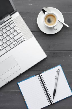 Çalışan bir kahve molasının portre görüntüsü. Laptop, kahve ve not defteriyle. Koyu bir ahşap arka planda.