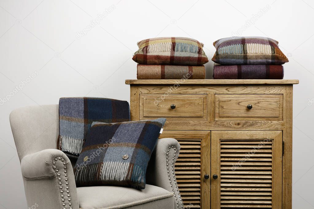 Chair and side cabinet with blue and maroon checked cushions and throws, against  a white background.