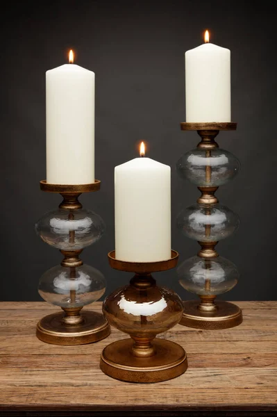 3 glass candle holders and glowing candles, shot on a wooden table, with a dark grey background