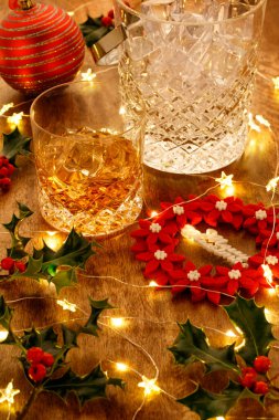 Kristal bardak viski ve Noel ışıkları ve takı süslemeleri olan bir buz kovası, ahşap arka planda.
