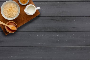 Besleyici bir kase yulaf lapası, küçük bir kase esmer şeker, bir sürahi süt ve ahşap bir kaşıkla bir kase altın şurup, koyu ahşap bir arka planda, kopyasına yer var.