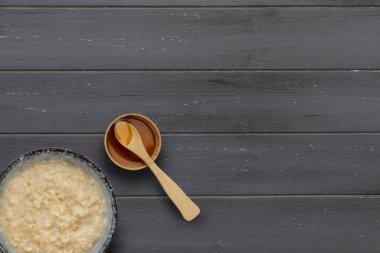 Besleyici bir kase yulaf lapası ve ahşap bir kaşıkla bir kase altın şurup. Koyu ahşap arka planda, kopyasına yer var.