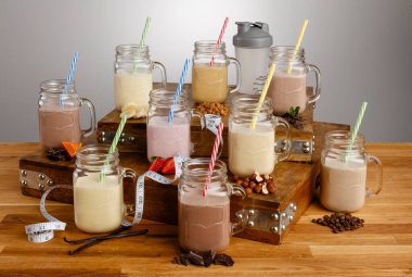 Çeşitli renkli milkshake ve malzemeler karıştırıcı ve mezura ölçer Mason kavanozlarında tahta bir masanın üzerinde kağıt kamışla