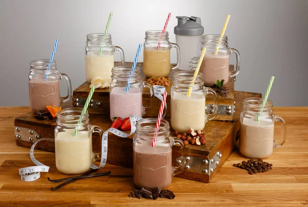 Çeşitli renkli milkshake ve malzemeler karıştırıcı ve mezura ölçer Mason kavanozlarında tahta bir masanın üzerinde kağıt kamışla