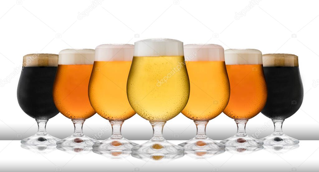 A row of refreshing lager, beer, cider and stout, in schooner glasses, with condensation, on a white table top and white background