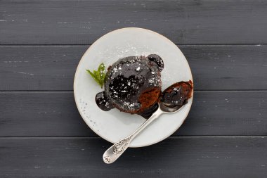 Yapışkan çikolata soslu, tek bir çikolatalı kek, beyaz bir tabakta, kaşıkla, koyu gri bir tahta yüzeyde fotokopi için yer var.