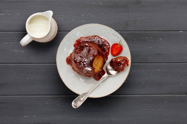 Çilekli kek, yapışkan çilek soslu, beyaz bir tabakta, bir kaşık ve bir sürahi kremayla, koyu gri ahşap bir yüzey üzerinde, kopyası için yer var.