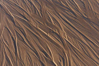 Islak kumlu bir plajdaki desenlere bakarak görüntüyü kapat. Dokuları, şekilleri ve 4 numaralı dalgalanmaları göster.