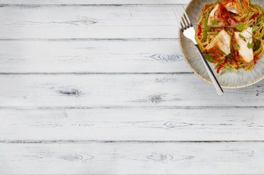 Lezzetli bir kase tavuklu chow mein, erişte ve sebze, kırsal bir kasede çatalla tedirgin beyaz ahşap arka planda.