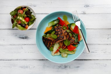 Lezzetli bir kase biftek fileto, tatlı patates püresi, kırmızı biber ve sebzeler, açık mavi bir kasede, bir yandan salata, sıkıntılı beyaz ahşap arka planda.