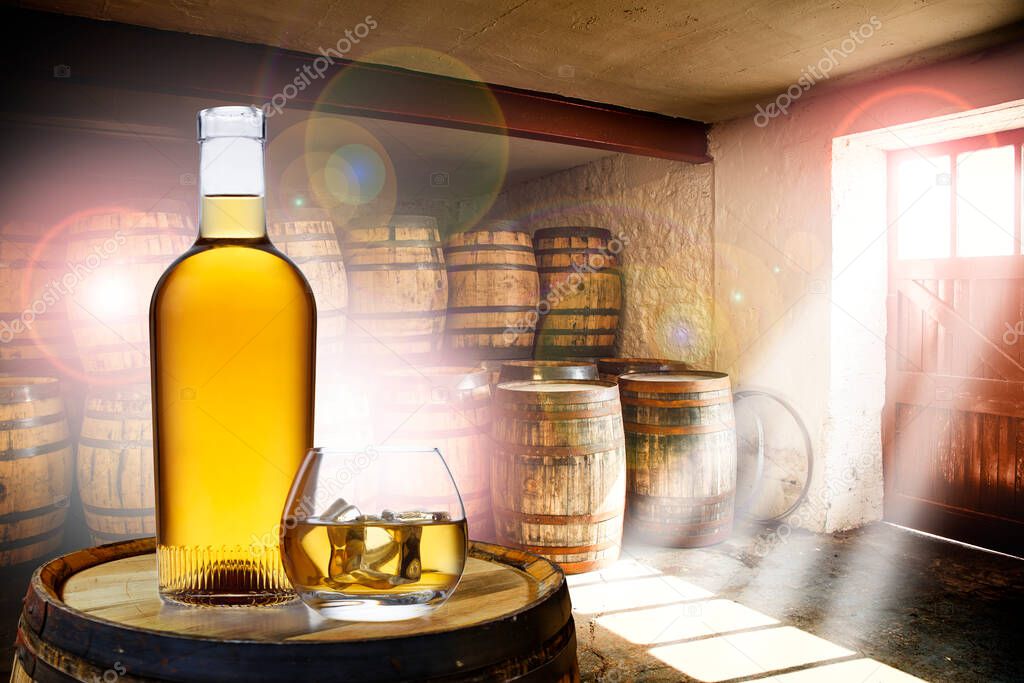 A bottle and glass of amber whisky set on top of an old barrel, in a barrel warehouse, with sun shining through the windows causing areas of lens flare.