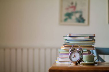 Colorful books and alarm clocks are placed on a wooden table in the house to prepare for online lessons from home and prevent coronavirus covid19 infection.Concepts for preparing books for learning clipart