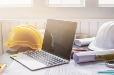 Mühendislerin ve mimarların masası planlar, kırtasiye malzemeleri ve bilgisayarlarla dolu. Ekipman, kırtasiye malzemeleri, bir sürü belge ve mühendisin masasına yerleştirilmiş bir kask..