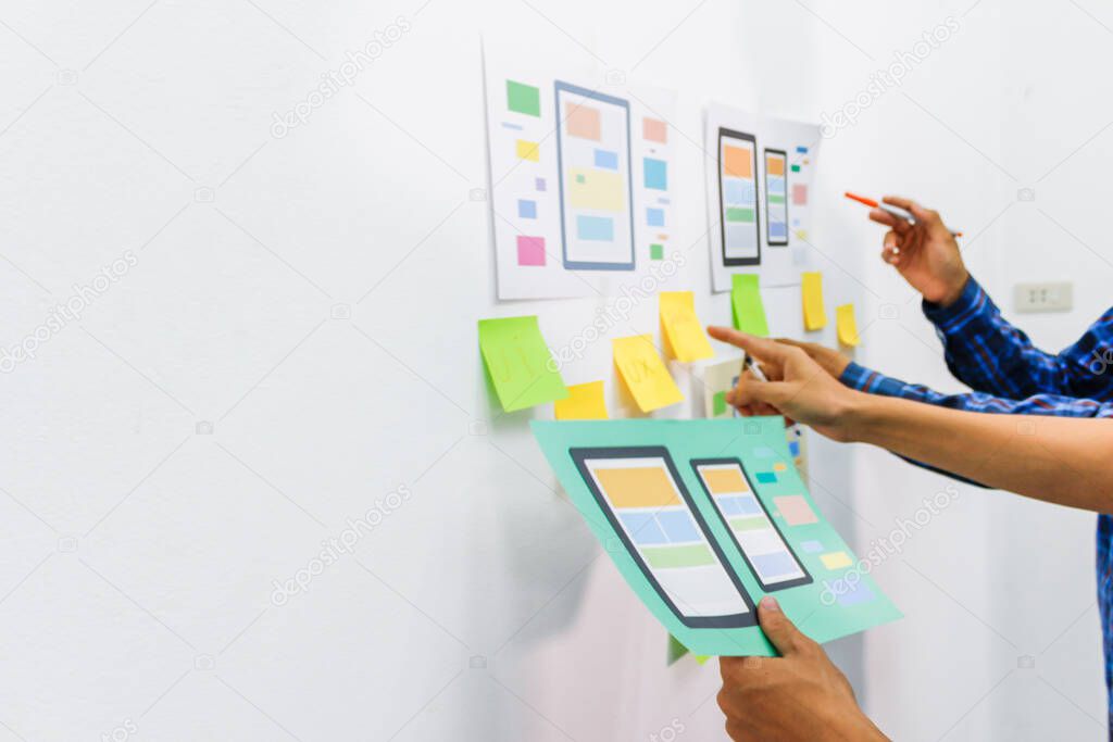 The team of website designers with the ux ui system are writing programs and laying the layer to determine the display style with the ux ui system within the front of the smartphone.