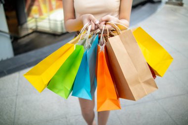 A young Asian woman holds several colorful shopping bags in her hands after going shopping in a shopping mall because of a holiday sale. Many colorful shopping paper bags in the hands of a young woman