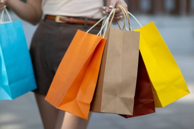 A young Asian woman holds several colorful shopping bags in her hands after going shopping in a shopping mall because of a holiday sale. Many colorful shopping paper bags in the hands of a young woman