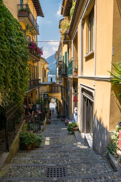 BELLAGIO, ITALY - 1 JULY 2018: Narrow alley of Bellagio leading to the lake, in the background a glimpse of the lake,Italy