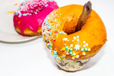 Üstünde donut olan bir kapuçino bardağı ve içine bir kaşık ve arka planda bir tabakta bir donut. Seçici odak.