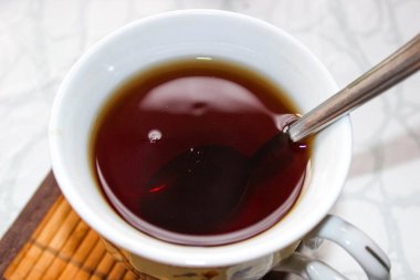 Elinde siyah çay kaşığı olan bir kupada. Kapat..