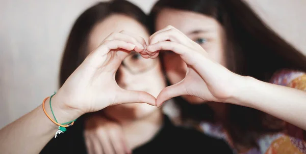 Two teenage girls make a heart out of their fingers and look through it. Selective focus.