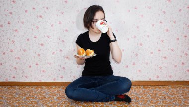 Yerde oturup çay içen ve sosisli yiyen güzel bir kız. Evin geri kalanı..