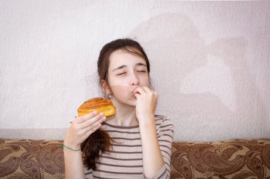 Genç bir kız elinde tatlı bir çörek tutuyor ve nefis bir jest yapıyor. Ortalama plan.