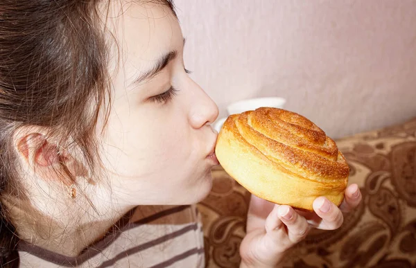 A teenage girl holds a sweet bun in her hand and shows that the bun is very tasty. Average plan.